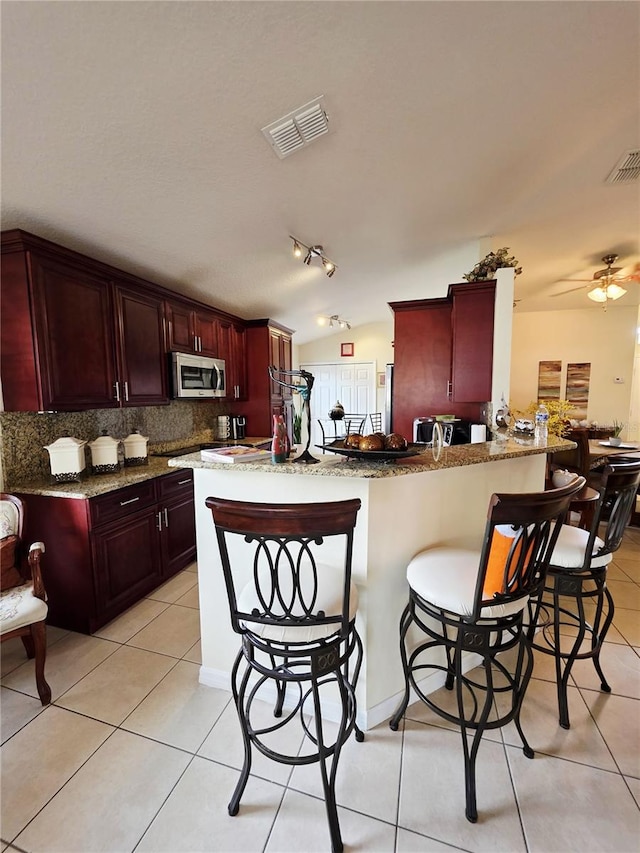 kitchen featuring tasteful backsplash, lofted ceiling, a kitchen breakfast bar, light tile patterned floors, and kitchen peninsula