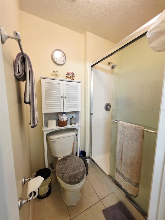 bathroom featuring tile patterned floors, toilet, a shower with door, and a textured ceiling