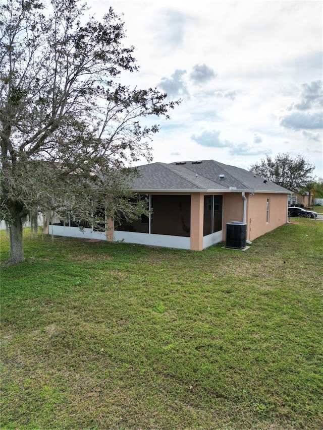 rear view of house featuring central AC unit, a sunroom, and a lawn