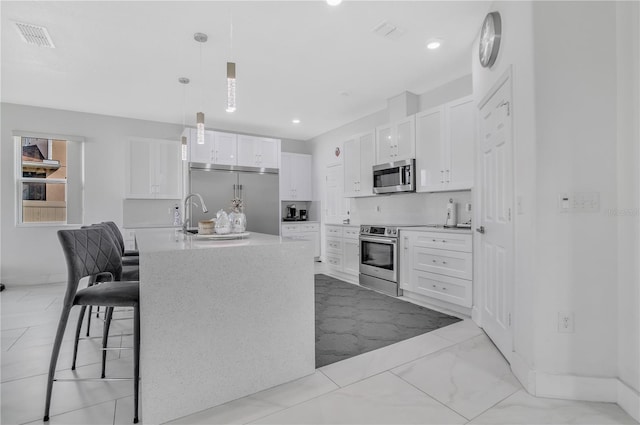 kitchen with white cabinets, a kitchen breakfast bar, hanging light fixtures, stainless steel appliances, and a center island with sink