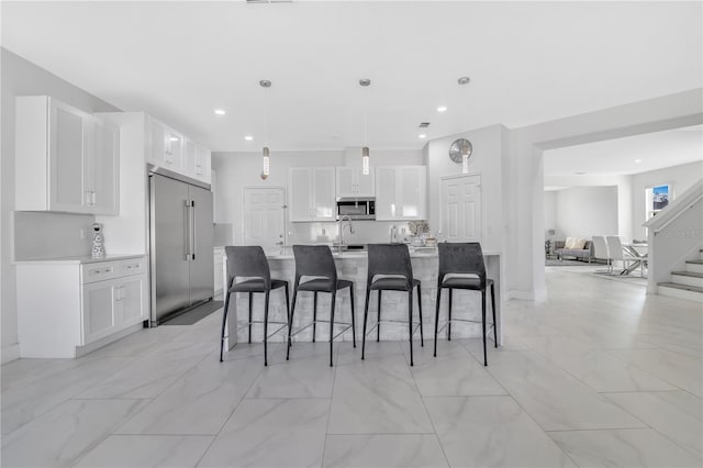 kitchen featuring stainless steel appliances, decorative light fixtures, a kitchen island with sink, and white cabinets