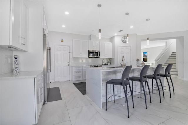 kitchen with decorative light fixtures, an island with sink, stainless steel appliances, decorative backsplash, and white cabinets