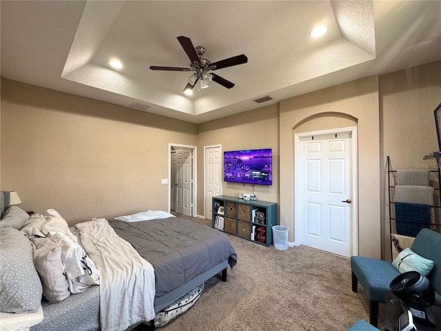 carpeted bedroom with a tray ceiling and ceiling fan