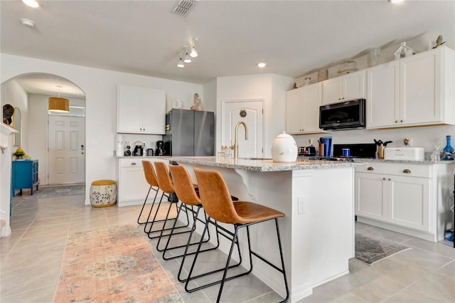 kitchen featuring sink, white cabinetry, a center island with sink, stainless steel refrigerator, and light stone countertops