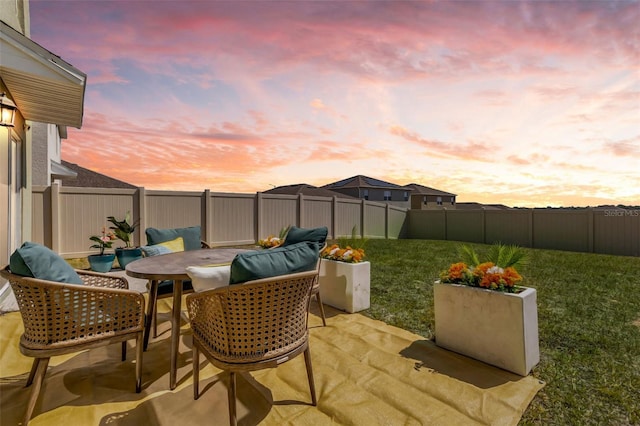 patio terrace at dusk featuring a lawn and a fenced backyard