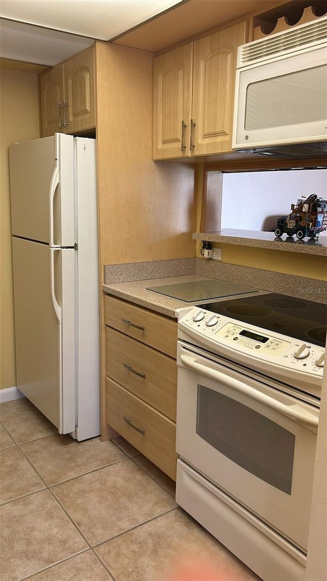 kitchen with light tile patterned floors, light brown cabinetry, and white appliances