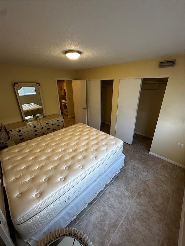 bedroom featuring light tile patterned flooring, a textured ceiling, and two closets