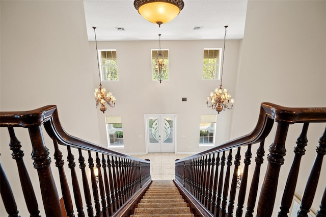 stairs featuring a towering ceiling, visible vents, baseboards, and a notable chandelier