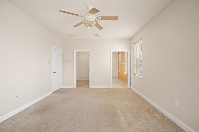 unfurnished bedroom with light carpet, baseboards, a ceiling fan, ensuite bathroom, and a spacious closet