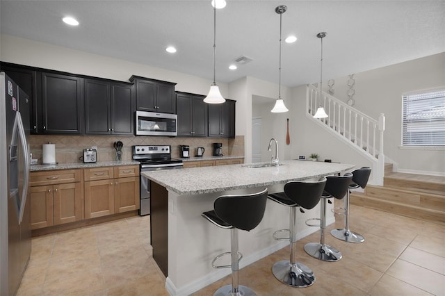 kitchen featuring sink, decorative light fixtures, appliances with stainless steel finishes, an island with sink, and light stone countertops