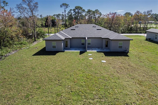 rear view of property with a shingled roof, stucco siding, a patio, and a lawn