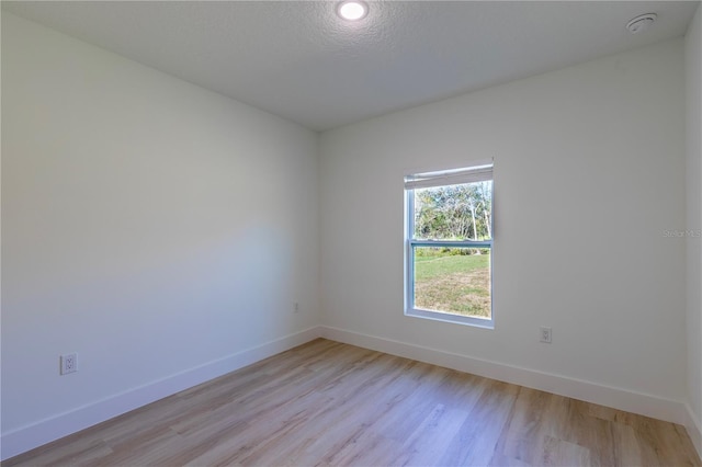 empty room with light wood-style floors, a textured ceiling, and baseboards