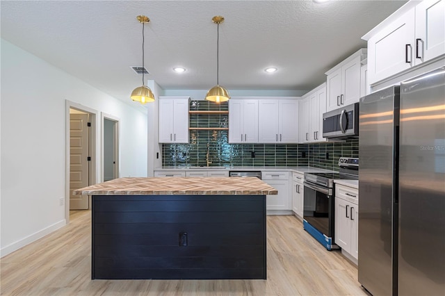 kitchen with butcher block countertops, a center island, decorative light fixtures, stainless steel appliances, and white cabinetry