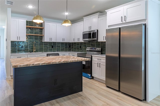 kitchen with appliances with stainless steel finishes, white cabinets, a sink, and decorative light fixtures