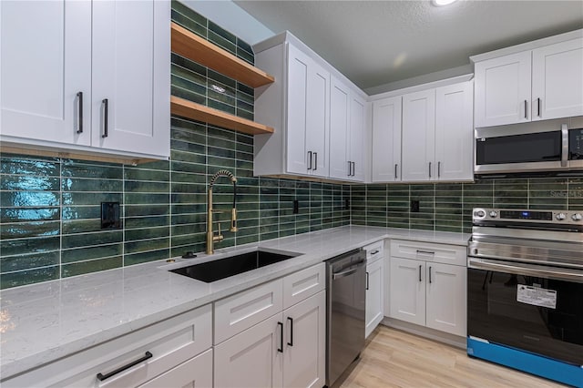 kitchen with light stone counters, stainless steel appliances, a sink, white cabinetry, and open shelves