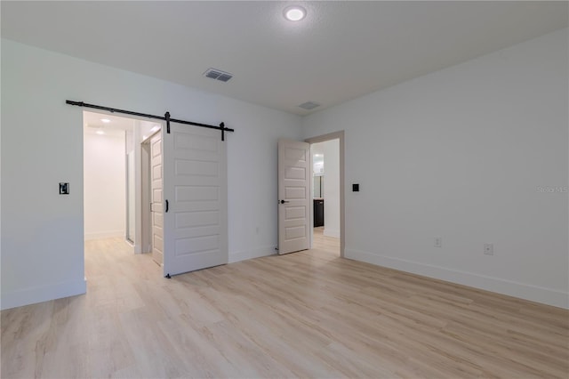 empty room featuring light wood-style floors, visible vents, baseboards, and a barn door