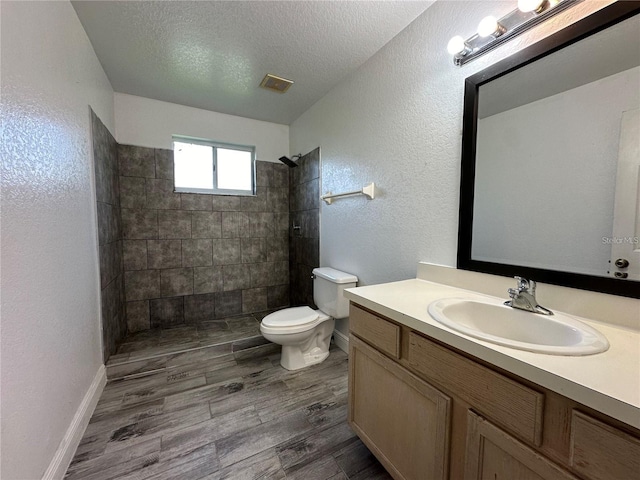 bathroom featuring hardwood / wood-style flooring, tiled shower, vanity, a textured ceiling, and toilet