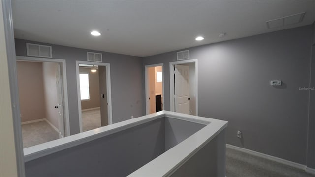 corridor with an upstairs landing, visible vents, and carpet floors