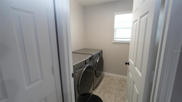 clothes washing area featuring baseboards, light tile patterned flooring, washing machine and dryer, and laundry area