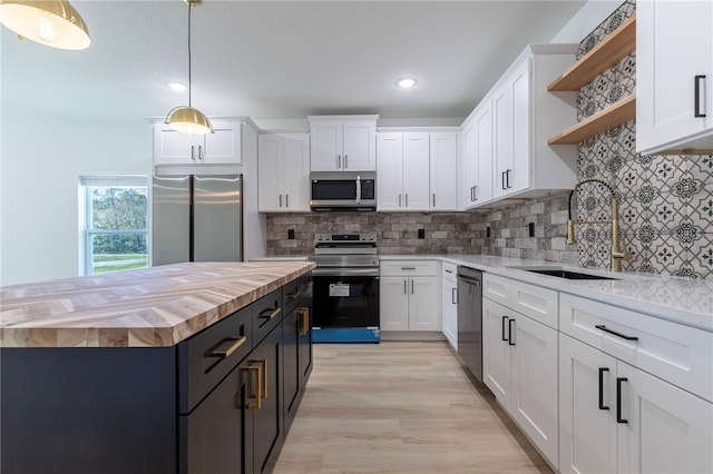 kitchen featuring open shelves, appliances with stainless steel finishes, white cabinets, a sink, and wood counters