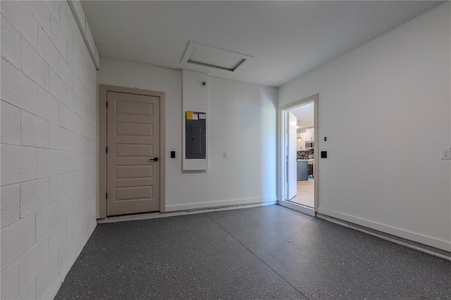 empty room with concrete block wall, attic access, electric panel, and speckled floor