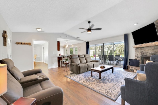 living room with ceiling fan with notable chandelier, a fireplace, lofted ceiling, a textured ceiling, and light hardwood / wood-style flooring