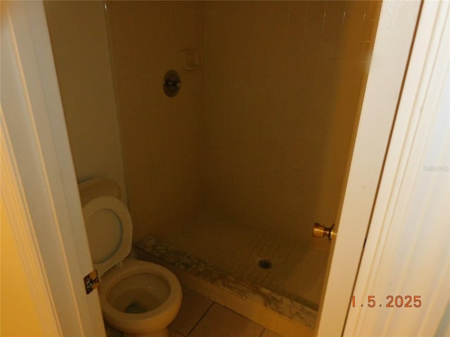 bathroom featuring tiled shower, toilet, and tile patterned flooring