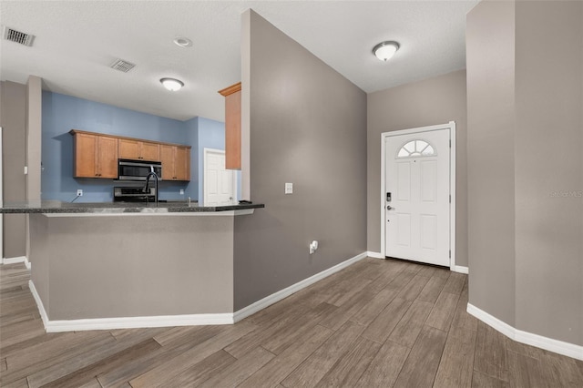 kitchen with baseboards, visible vents, stainless steel microwave, brown cabinets, and wood finished floors