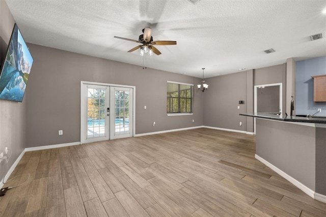 unfurnished living room featuring ceiling fan with notable chandelier, french doors, light wood-type flooring, and visible vents