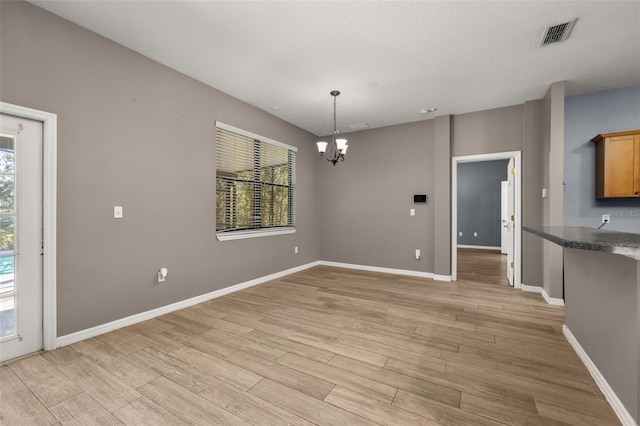 unfurnished dining area with a chandelier, light wood finished floors, visible vents, and baseboards