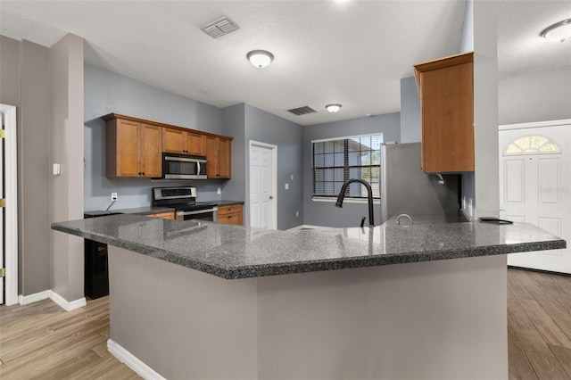 kitchen with stainless steel appliances, light wood-style flooring, brown cabinetry, and visible vents