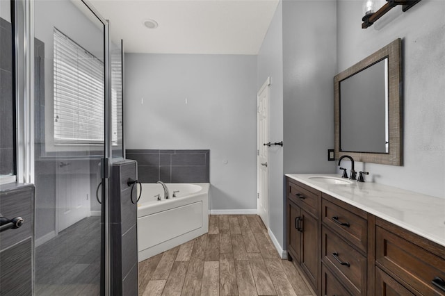 bathroom with baseboards, wood finished floors, vanity, a shower stall, and a bath