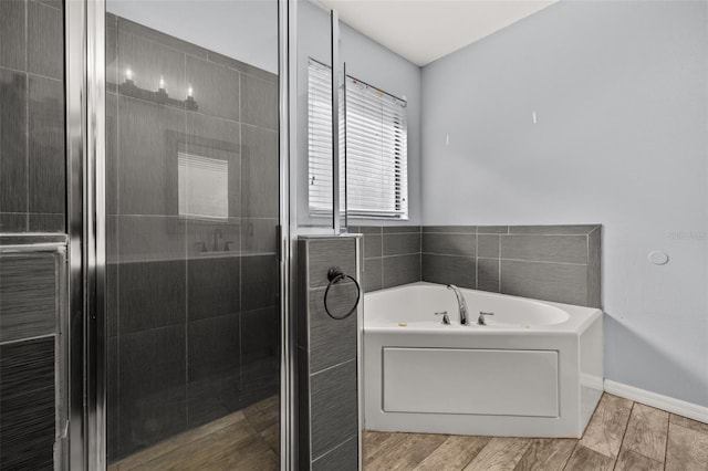 bathroom featuring a stall shower, wood finish floors, baseboards, and a bath