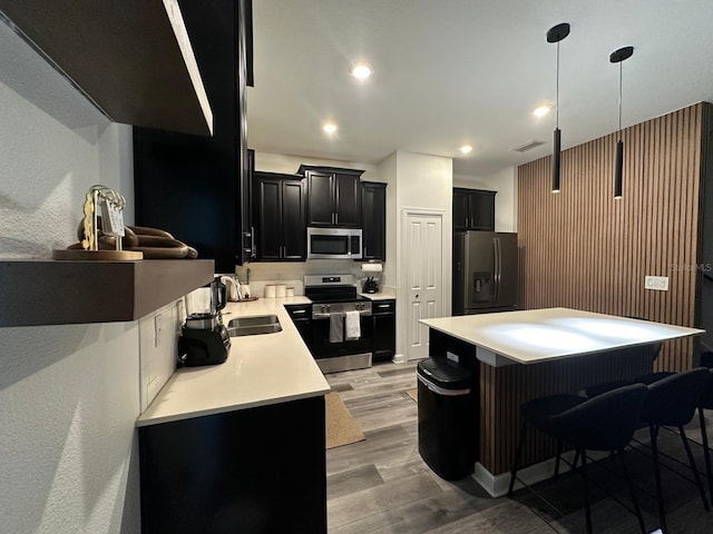 kitchen featuring sink, stainless steel appliances, a kitchen bar, decorative light fixtures, and light wood-type flooring