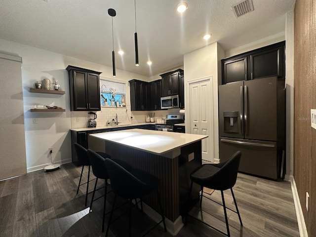 kitchen featuring hanging light fixtures, appliances with stainless steel finishes, a center island, and dark wood-type flooring