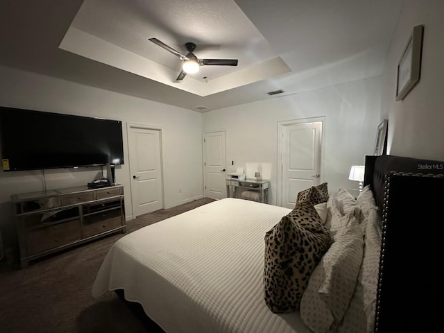 bedroom with ceiling fan, a tray ceiling, and dark colored carpet