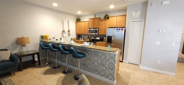 kitchen featuring light tile patterned flooring, appliances with stainless steel finishes, backsplash, a kitchen bar, and kitchen peninsula