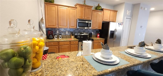 kitchen featuring stainless steel appliances, a kitchen breakfast bar, light stone counters, and decorative backsplash