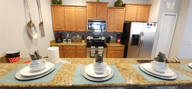 kitchen with stainless steel appliances, light stone countertops, and backsplash