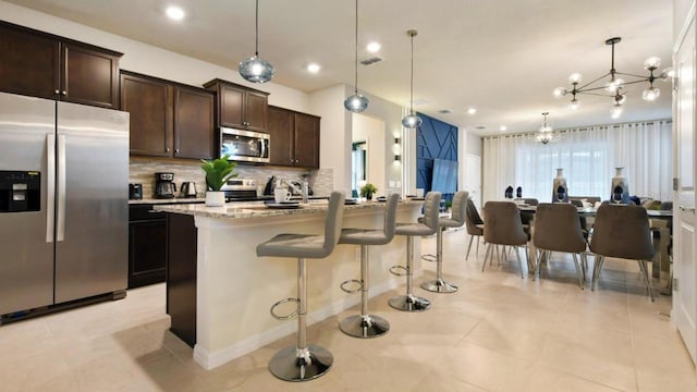 kitchen featuring an island with sink, a kitchen breakfast bar, hanging light fixtures, light stone counters, and stainless steel appliances