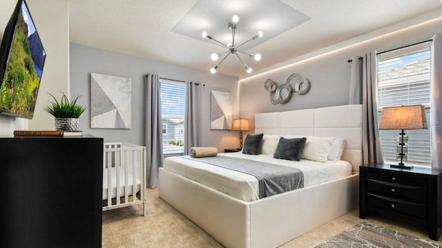 carpeted bedroom with multiple windows, an inviting chandelier, and a tray ceiling