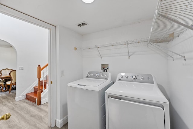 clothes washing area with arched walkways, visible vents, separate washer and dryer, light wood-type flooring, and laundry area