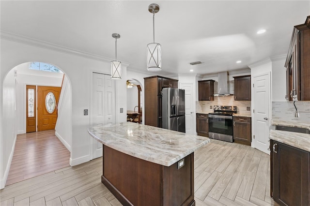 kitchen featuring appliances with stainless steel finishes, arched walkways, wall chimney exhaust hood, and tasteful backsplash