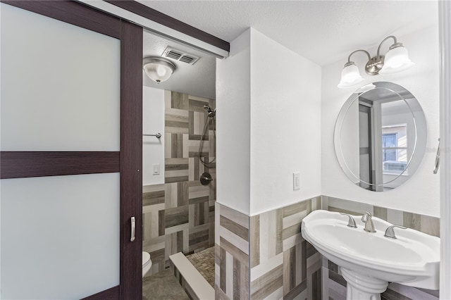 full bath featuring visible vents, a tile shower, a textured ceiling, and a sink