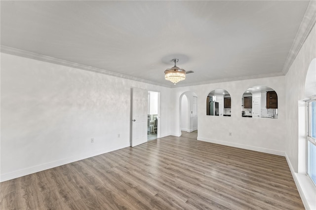 empty room with arched walkways, baseboards, wood finished floors, and crown molding