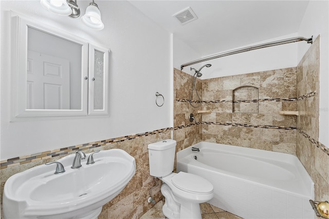 full bathroom featuring tile patterned floors, toilet, sink, tiled shower / bath, and tile walls