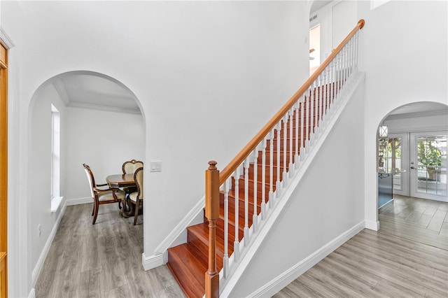 stairs with arched walkways, french doors, wood finished floors, and crown molding