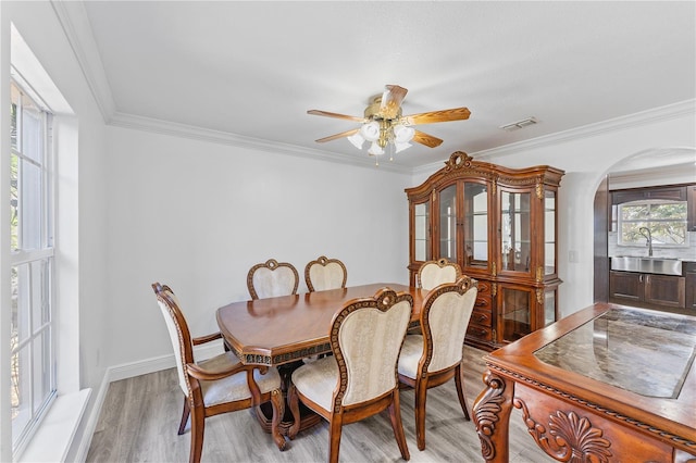 dining area with arched walkways, a ceiling fan, visible vents, light wood-type flooring, and crown molding