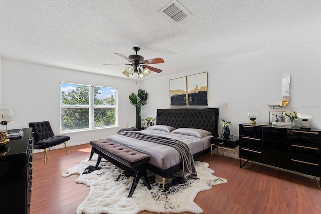 bedroom with a textured ceiling, dark wood-type flooring, visible vents, and baseboards