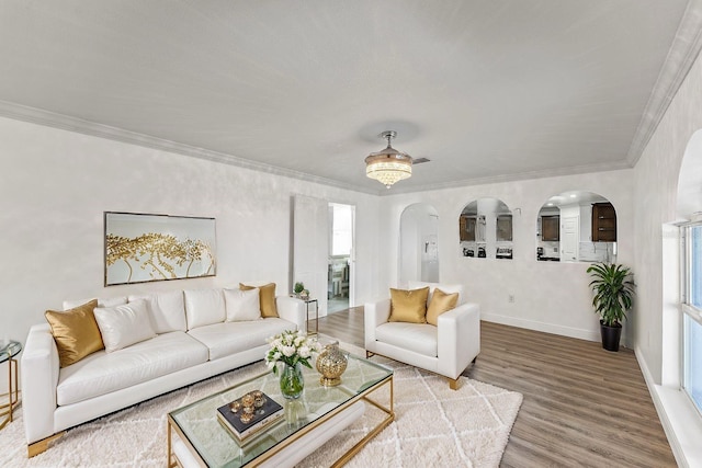 living room with baseboards, crown molding, arched walkways, and wood finished floors